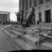 Stark black and white image of city stairs strewn with cardboard crosses and coffins at vigil for contruction workers in the Music CIty