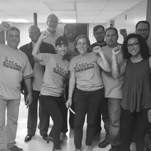 Group of people wearing Stand Up Nashville shirts, smiling widely and raising triumphant fists into the air