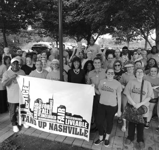 Groupd of happy and excited members of the community wearing Stand Up Nashville t-shirts and standing under trees holding Stand Up Nashville banner
