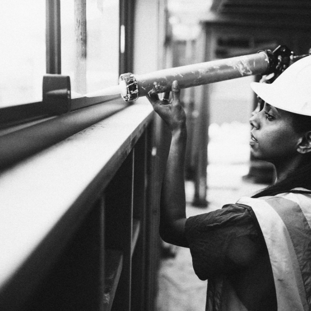 Female BPOC construction worker sealing the frame of a window in a big building
